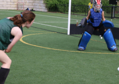 Girl hitting hockey ball at goalkeeper